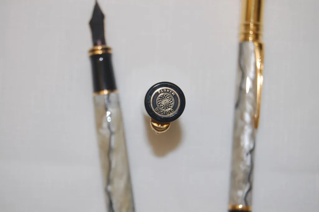 Close-up of a Parker Duofold cap medallion between pearl-pattern writing instruments